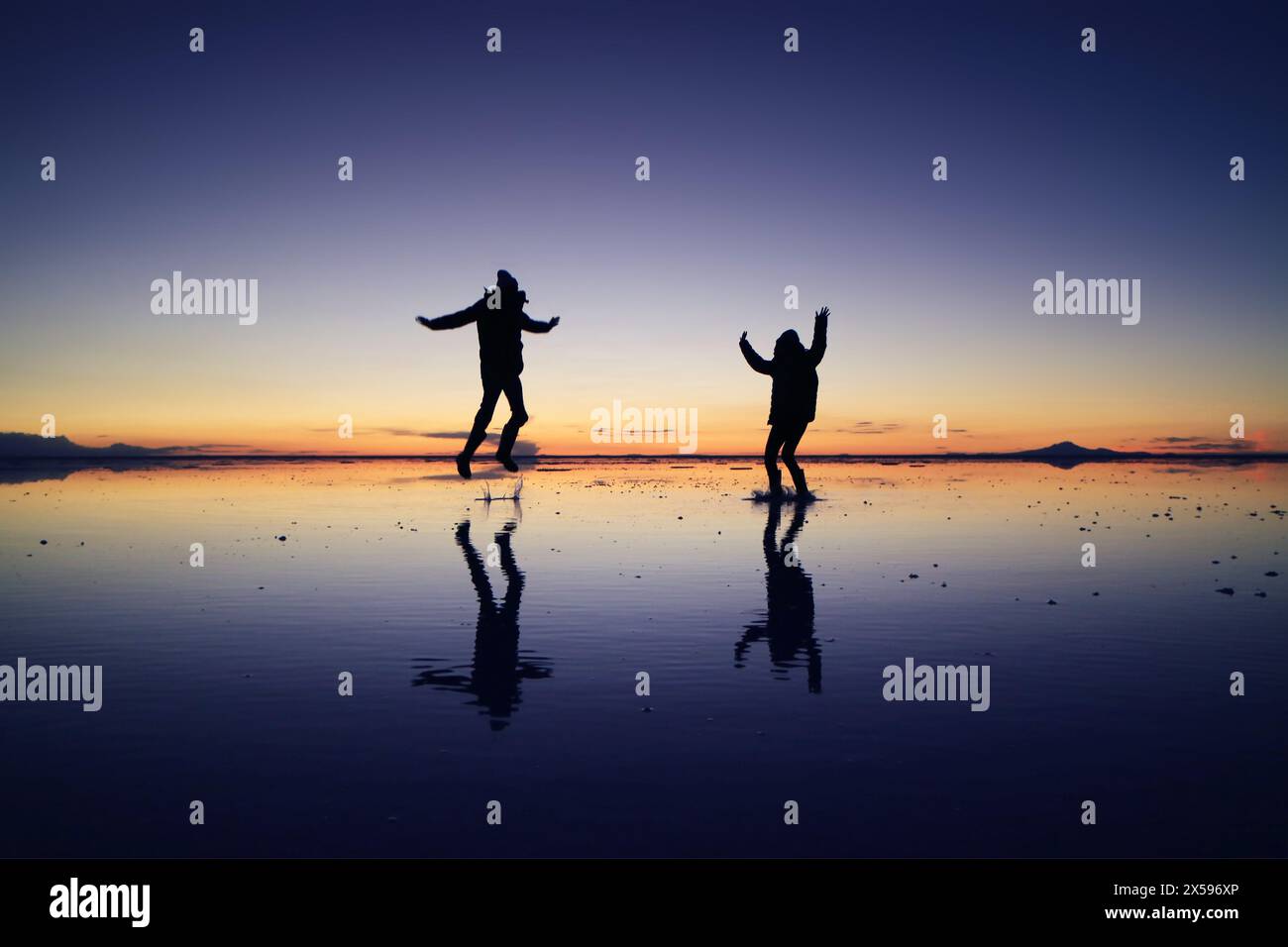 Silhouette di una coppia felice che salta sullo specchio dell'incredibile effetto delle distese saline di Uyuni contro il cielo del tramonto, Bolivia, Sud America Foto Stock