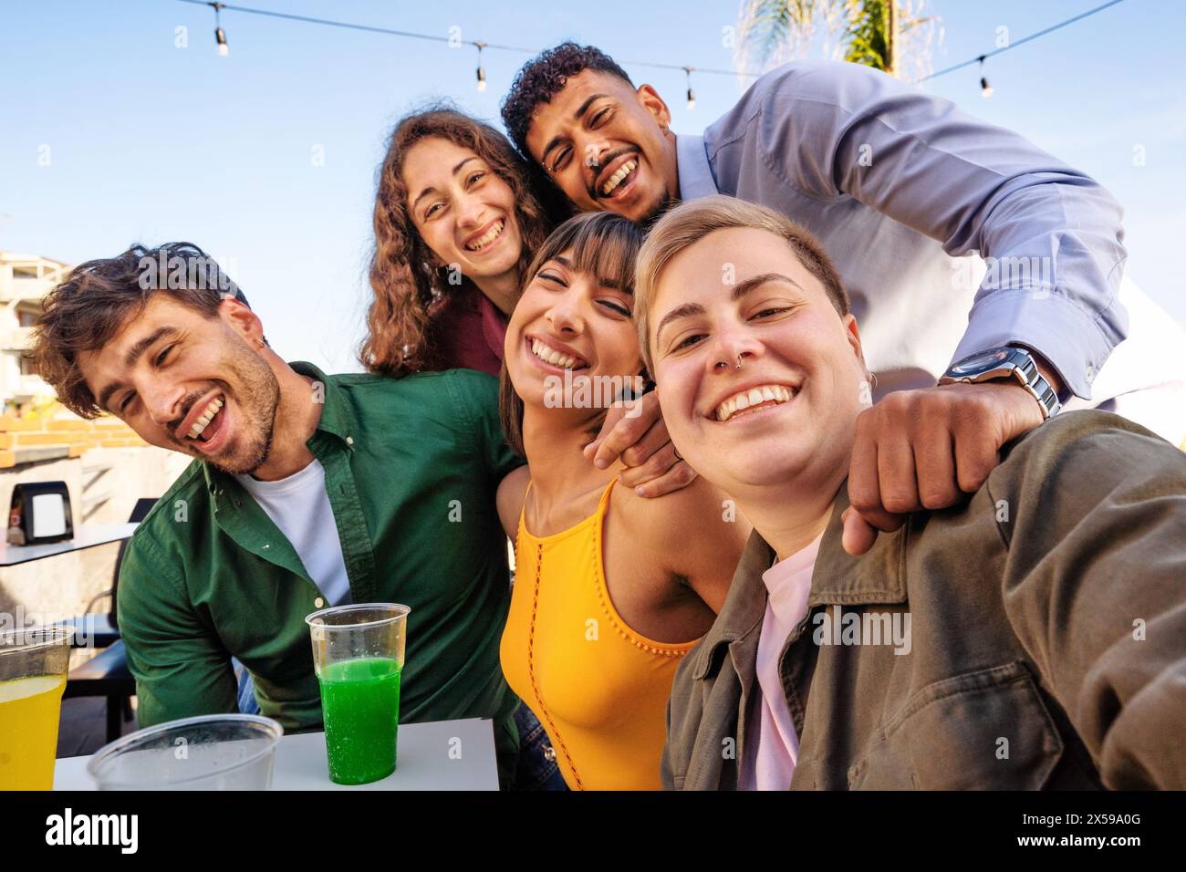Gruppo di amici diversi - ridendo e gustando un drink in una riunione sulla spiaggia, mostrando gioia e solidarietà in un ambiente informale all'aperto. Foto Stock