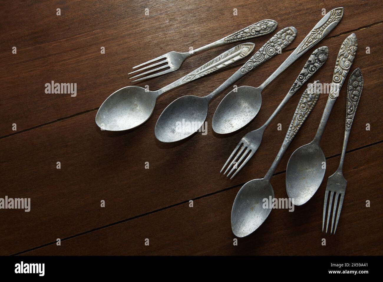 Diversi vecchi cucchiai e forchette in argento con ornamenti antichi sui manici su un tavolo di legno Foto Stock