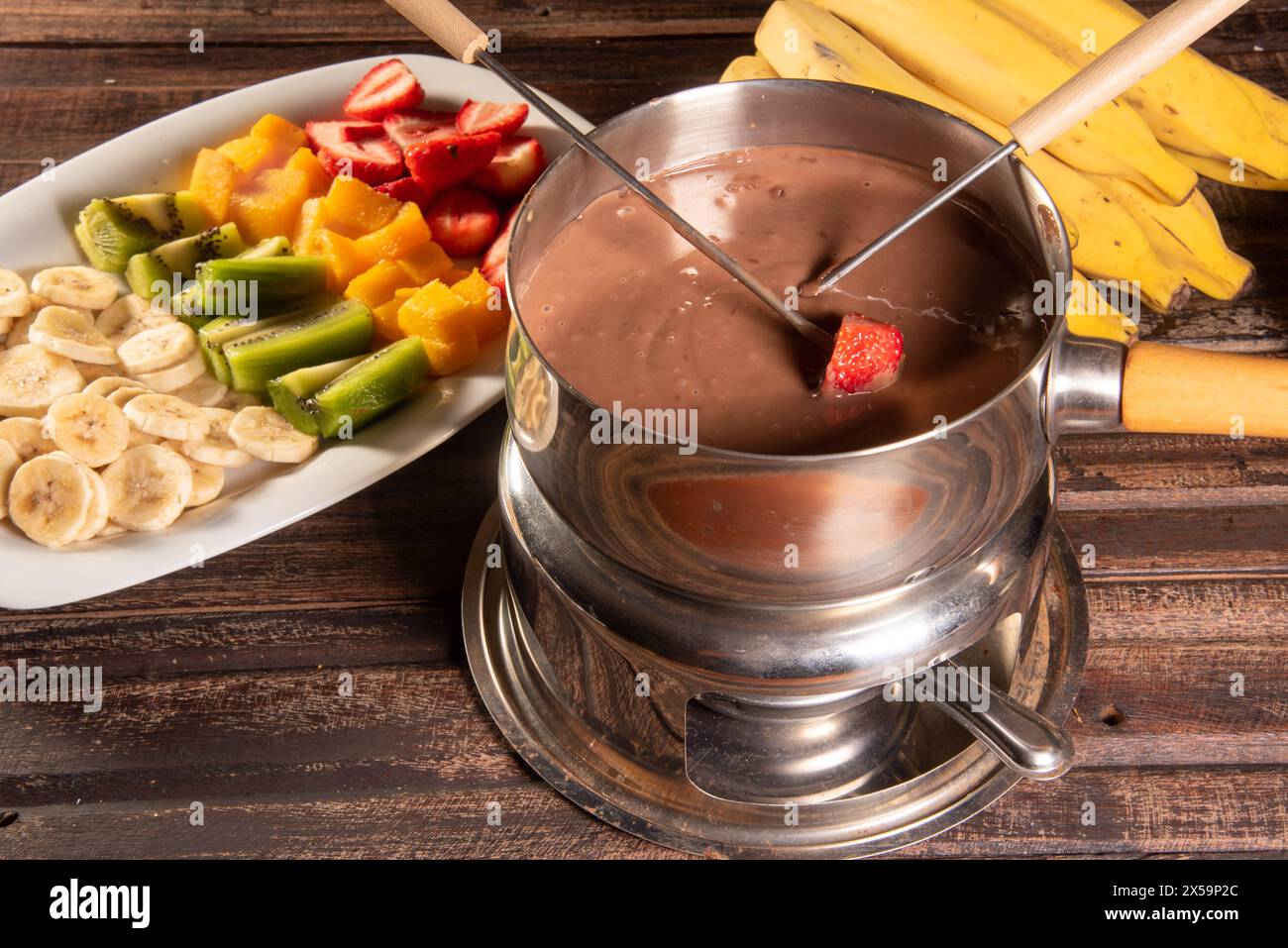 fonduta al cioccolato accompagnata da frutta tropicale su tavola di legno e sfondo scuro Foto Stock