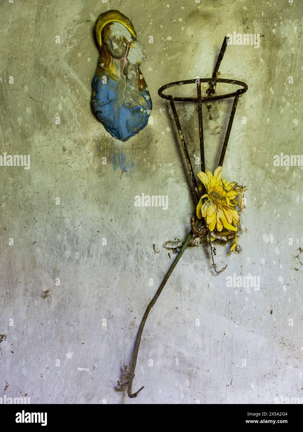 Un piccolo santuario sacro abbandonato, con l'immagine di nostra Signora ora sbucciata e scolorita, e una gerbera tristemente appassita. Foto Stock