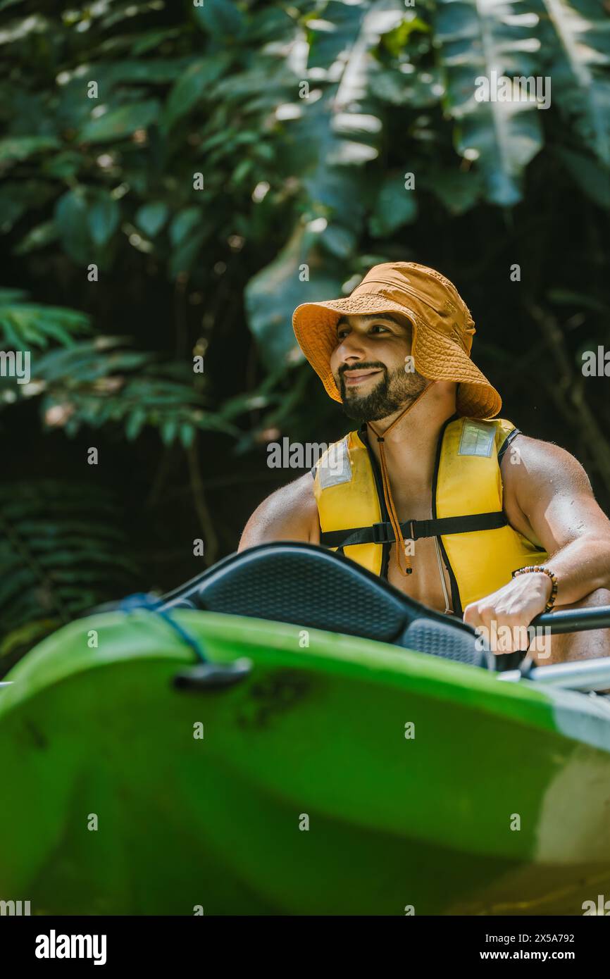 Uomo con giubbotto di salvataggio giallo e cappello da secchio che si prepara a fare kayak nella lussureggiante giungla della Costa Rica Foto Stock