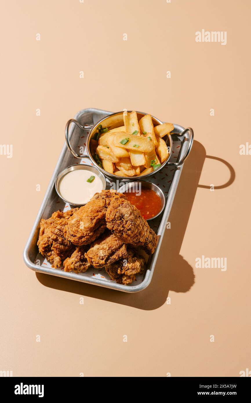 Deliziose ali di pollo fritte accompagnate da spicchi di patate dorate servite con salse cremose e piccanti. Foto Stock