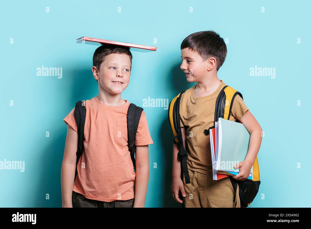 Un ragazzo con un libro in testa si distoglie lo sguardo, accanto al suo amico che tiene i libri e lo guarda. Foto Stock