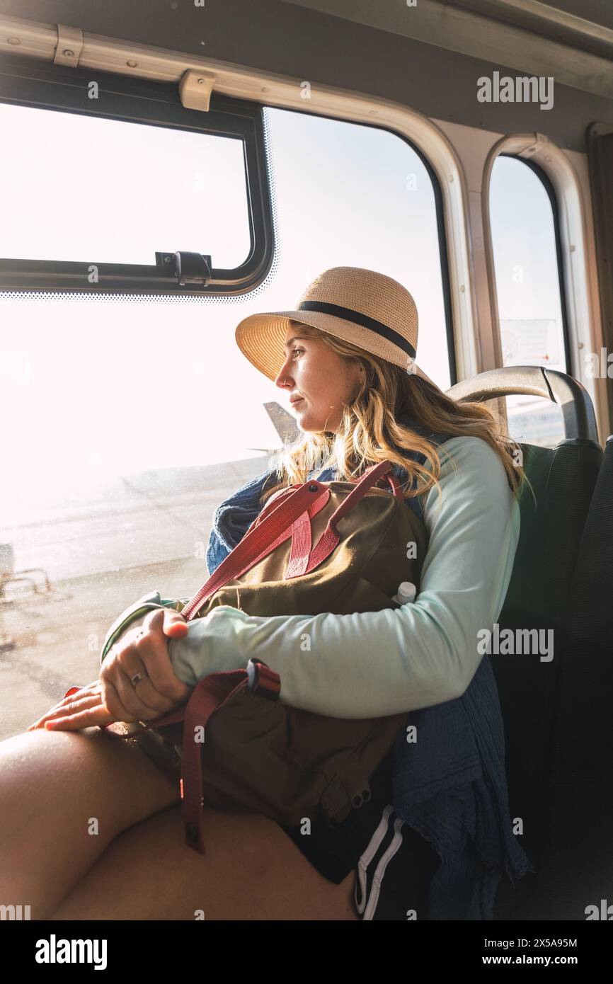 Una giovane donna premurosa guarda fuori dal finestrino di un autobus, il suo sguardo lontano e riflessivo mentre la luce del sole bagna gli interni. Foto Stock