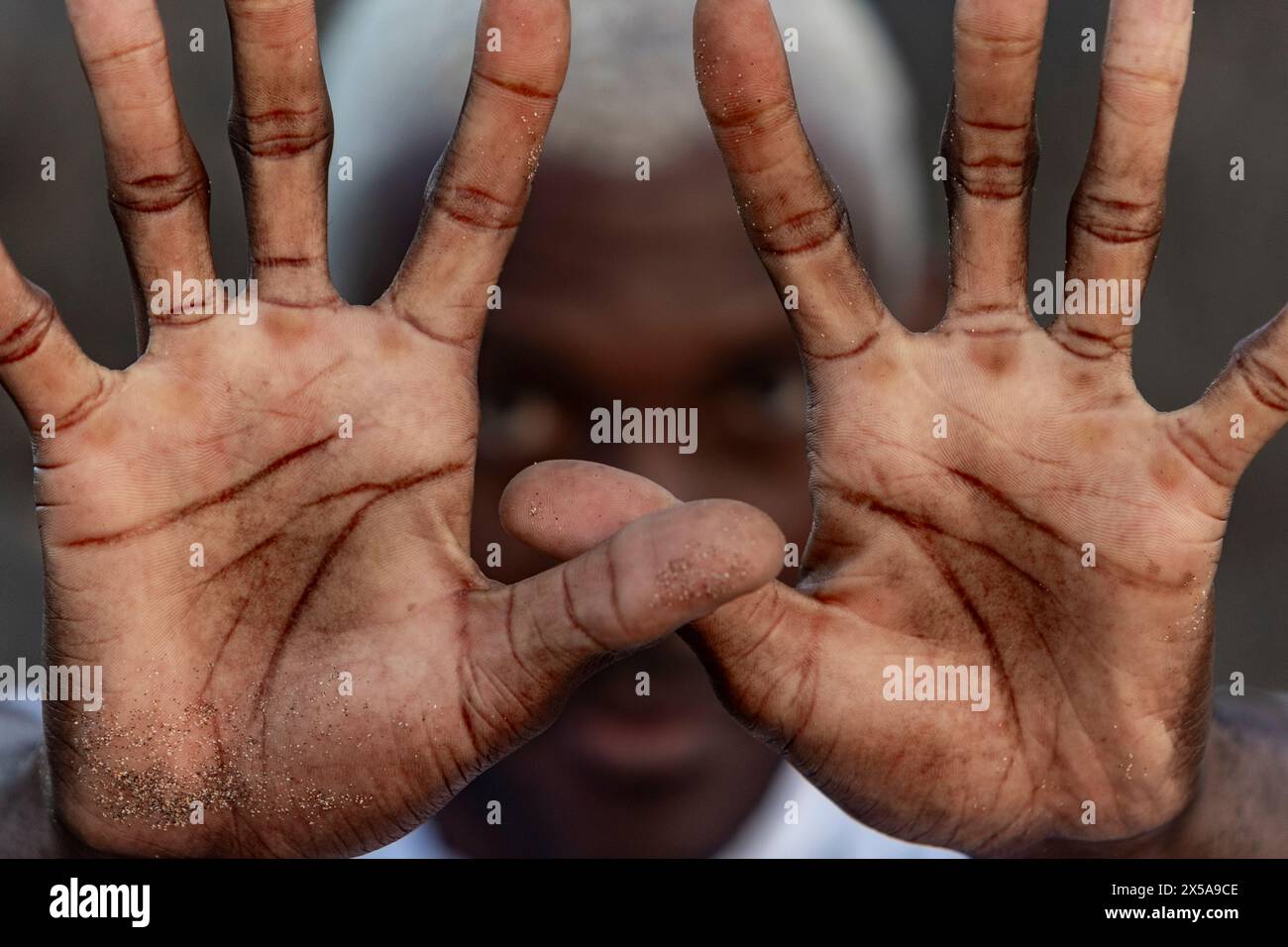 Un accattivante primo piano di un uomo con palme sabbiose che incornicia il suo sguardo intenso, mettendo in risalto le linee e le texture uniche della sua pelle Foto Stock
