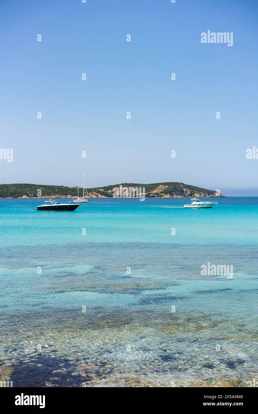 Acque turchesi cristalline con imbarcazioni da diporto al largo della costa sarda, che evocano un ambiente sereno e lussuoso, la spiaggia grande Pevero Foto Stock