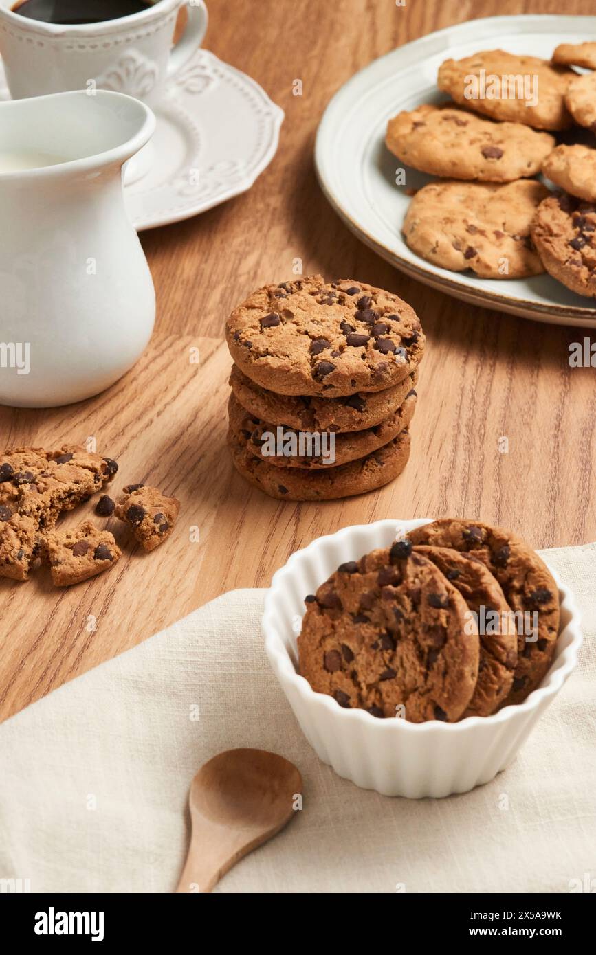 Una vista dall'alto di gustosi biscotti con scaglie di cioccolato su un tavolo di legno, accompagnati da stoviglie in ceramica bianca Foto Stock