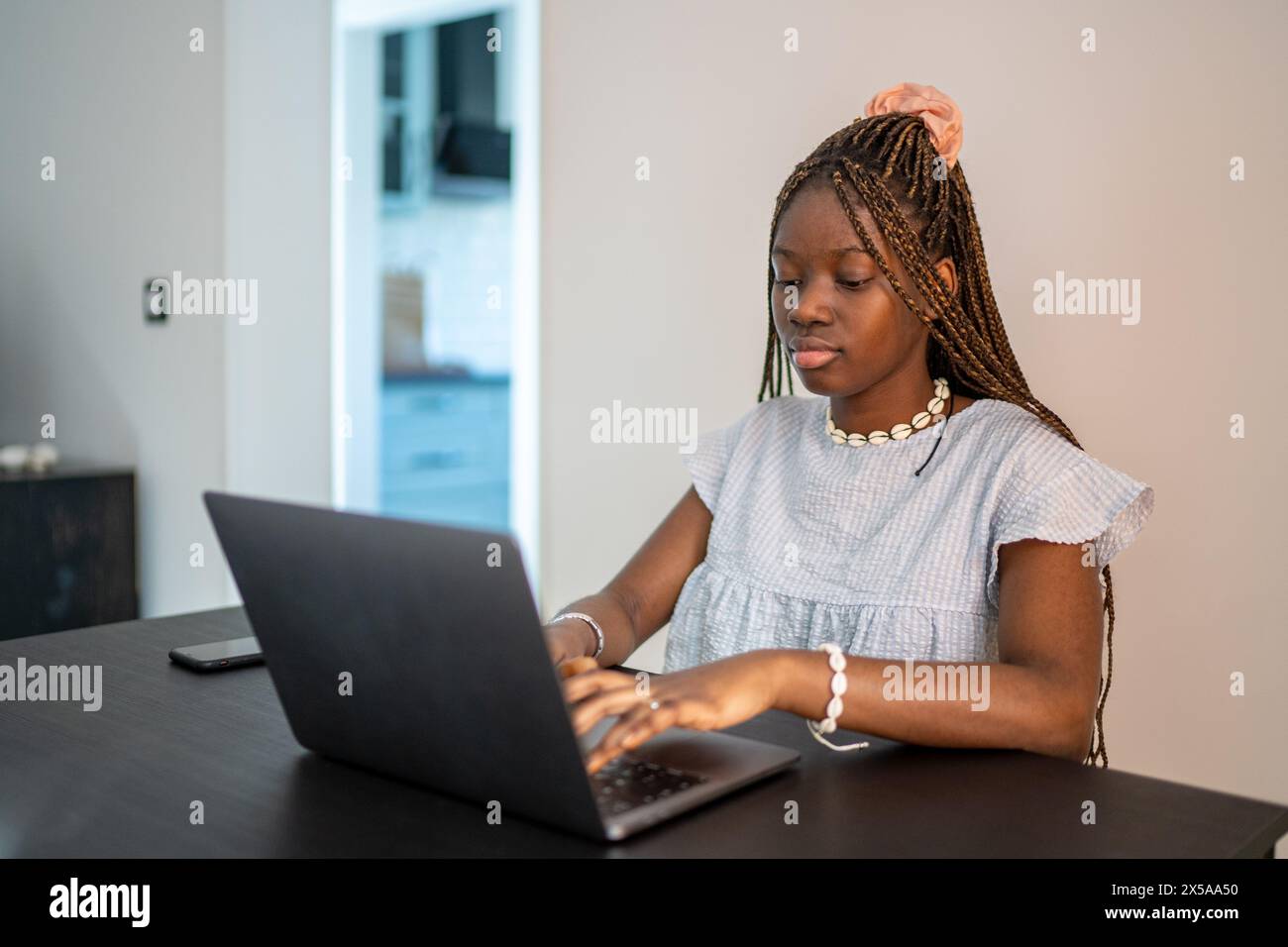 Una donna afroamericana si è concentrata sul suo lavoro mentre utilizza un computer portatile a casa, illustrando lo stile di vita del telelavoro Foto Stock
