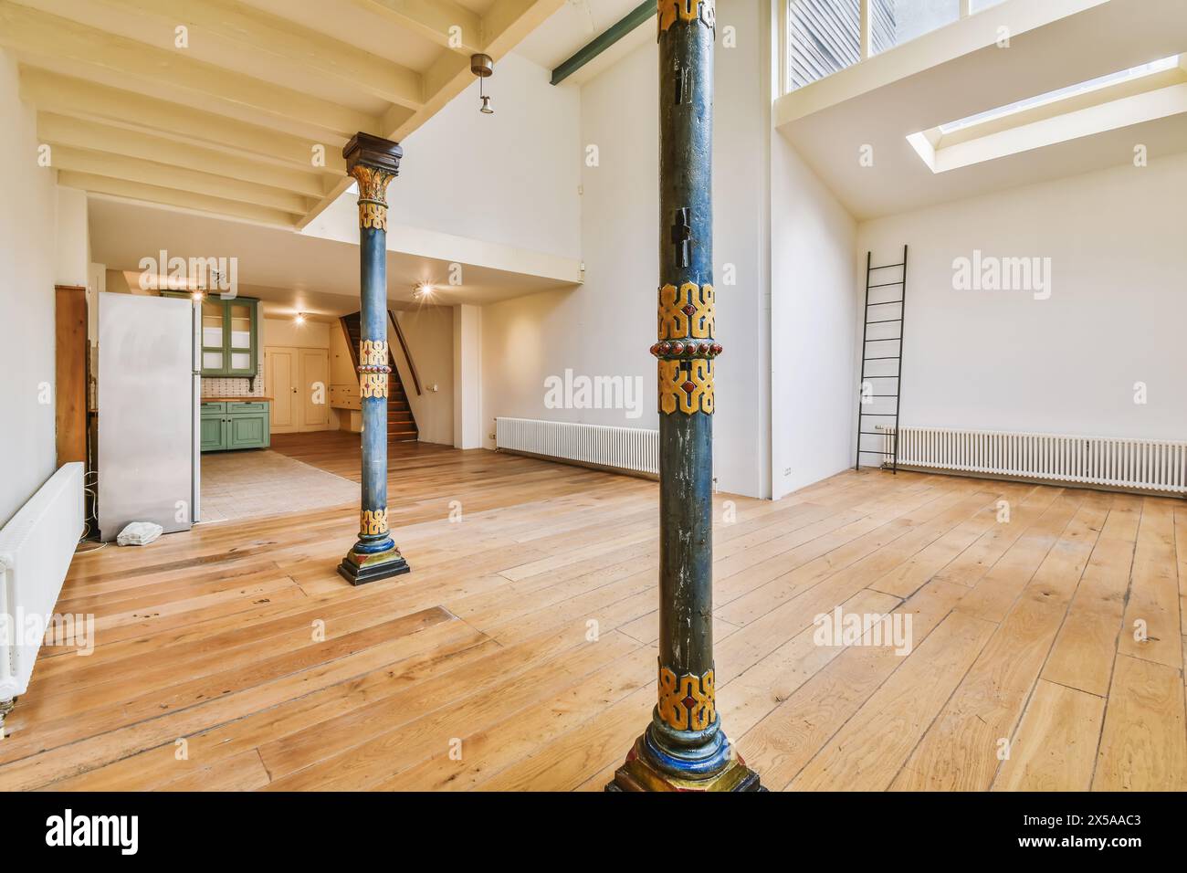 Una camera ampia e ben illuminata con pavimenti in legno duro, una colonna ornamentale dipinta e una scala in stile loft. Foto Stock