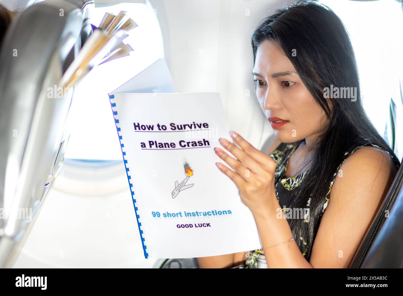La donna spaventata in aereo sta studiando le istruzioni di sopravvivenza all'incidente Foto Stock