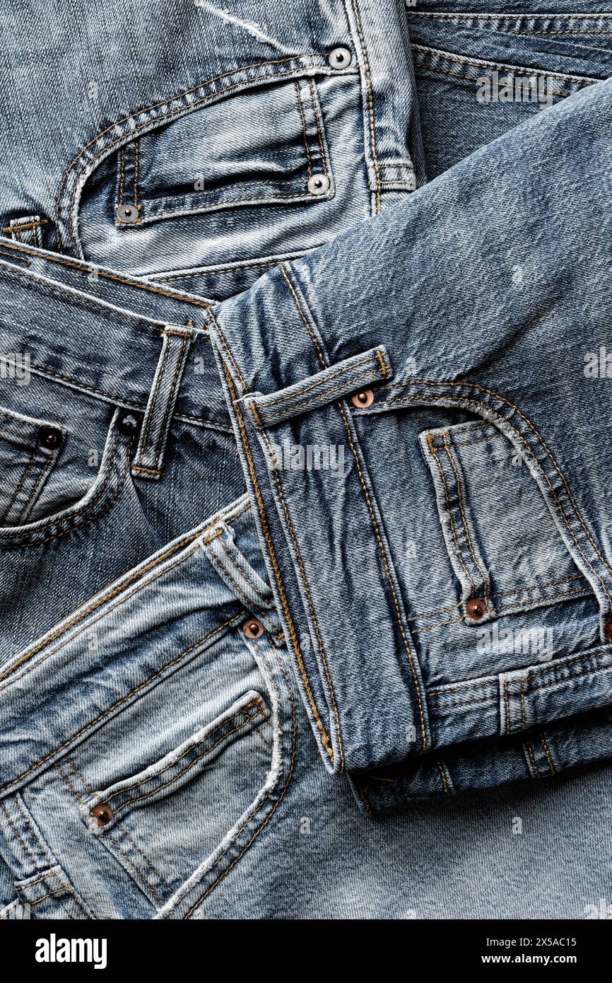 Gruppo di jeans in denim invecchiati, disposti su fondo in tessuto blu astratto, foto ravvicinata Foto Stock