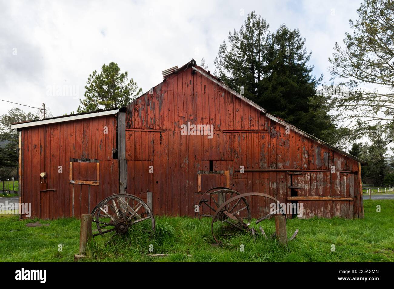 Vecchia, vecchia, rossa, baracca in legno e ruote di carri d'epoca rotte nella California rurale settentrionale. Foto Stock