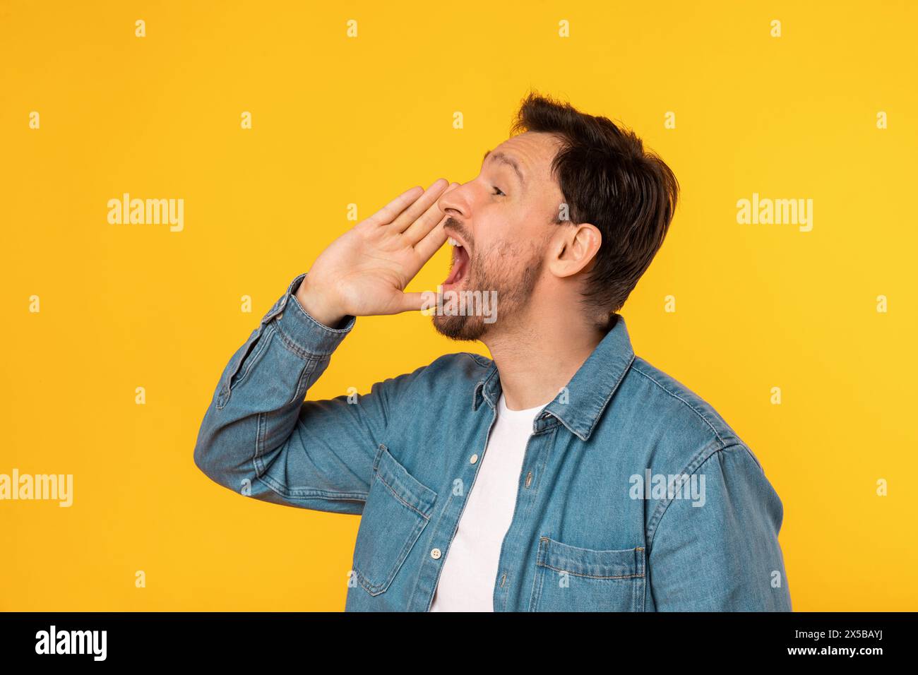 Camicia Young Man in denim che grida annuncio su sfondo giallo Foto Stock