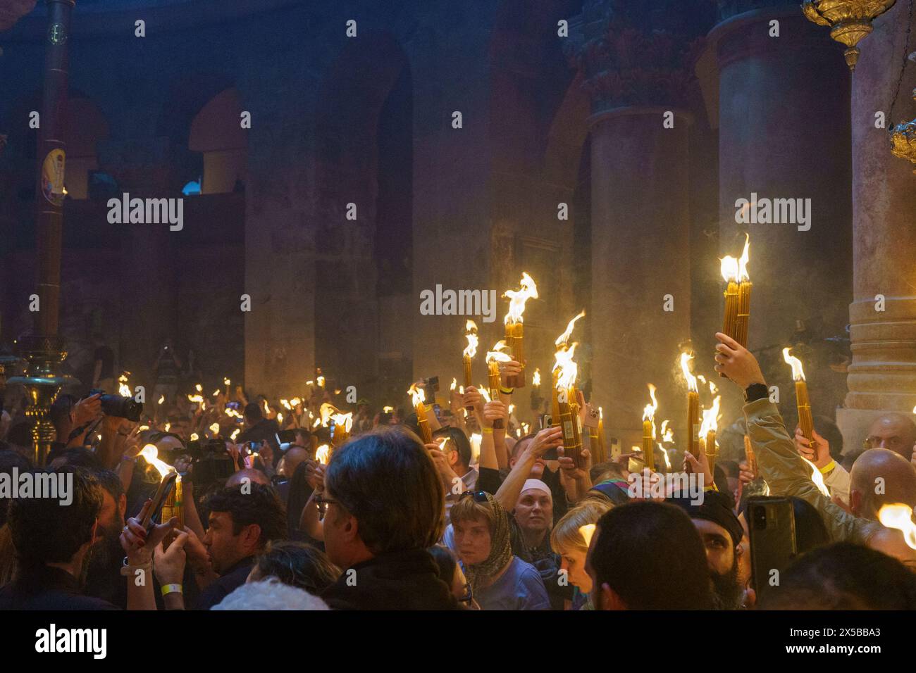 La luce Santa è condivisa tra i devoti, dalla candela alla candela, e presto la chiesa è piena di candele. I devoti cantano, lodano il miracolo e scattano selfie con il fuoco santo. La cerimonia del Santo fuoco è celebrata dalle chiese ortodosse nella Chiesa del Santo Sepolcro di Gerusalemme ogni anno prima della Pasqua. Questo evento spirituale e religioso è uno dei rituali più importanti del cristianesimo ortodosso e molti pellegrini si riuniscono da tutto il mondo per testimoniarlo. Durante la cerimonia il Patriarca greco entra nelle edicole dove si trova la tomba di Gesù, pregando fino al santo Foto Stock