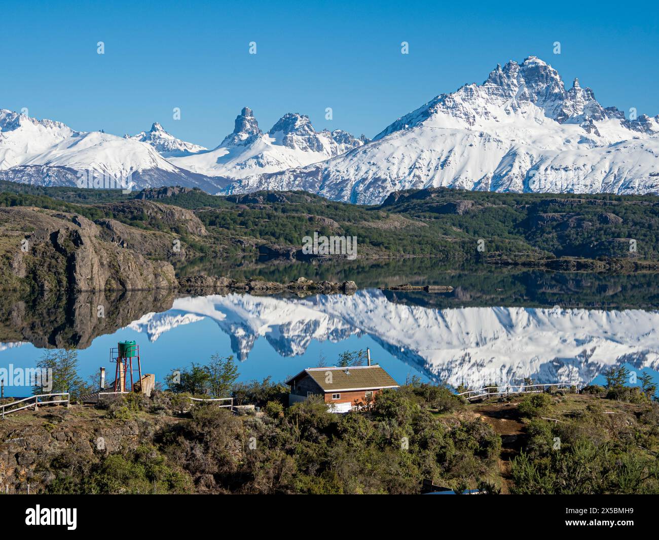 Il monte innevato Cerro Castillo si riflette in un lago, una piccola fattoria vicino al lago, Patagonia, Cile Foto Stock