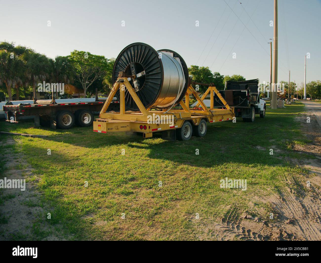 Avvolgicavo per avvolgicavo giallo con un grande rotolo di filo nel campo erba della sottostazione elettrica con un camion bianco e pali in acciaio Foto Stock Avvolgicavo per avvolgicavo giallo con un grande rotolo di filo nel campo erba della sottostazione elettrica con un camion bianco e pali in acciaio Foto Stock