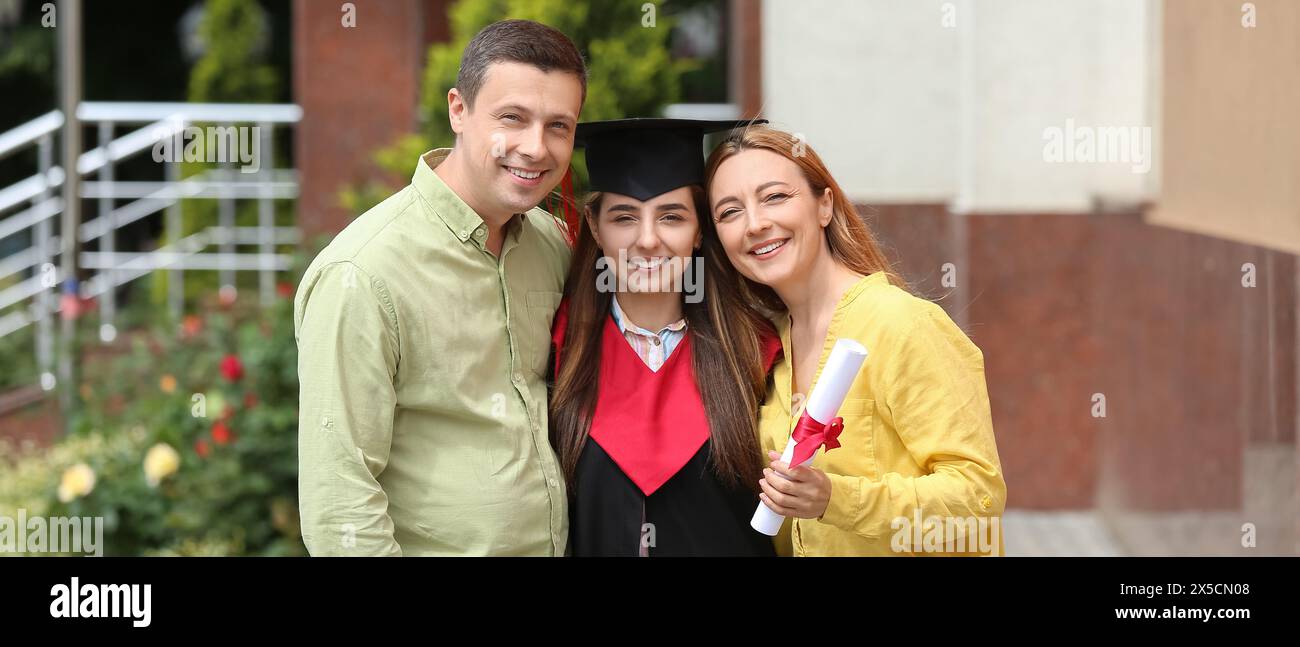 Felice studentessa laureata con i genitori all'aperto Foto Stock