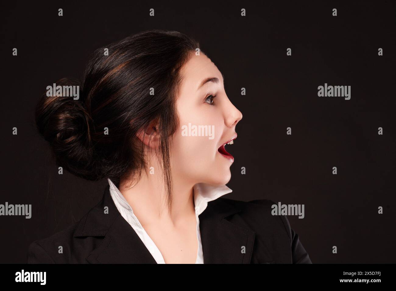 La giovane professionista espressiva mostra una reazione spontanea di sorpresa, la sua espressione facciale è vivida sullo sfondo scuro Foto Stock