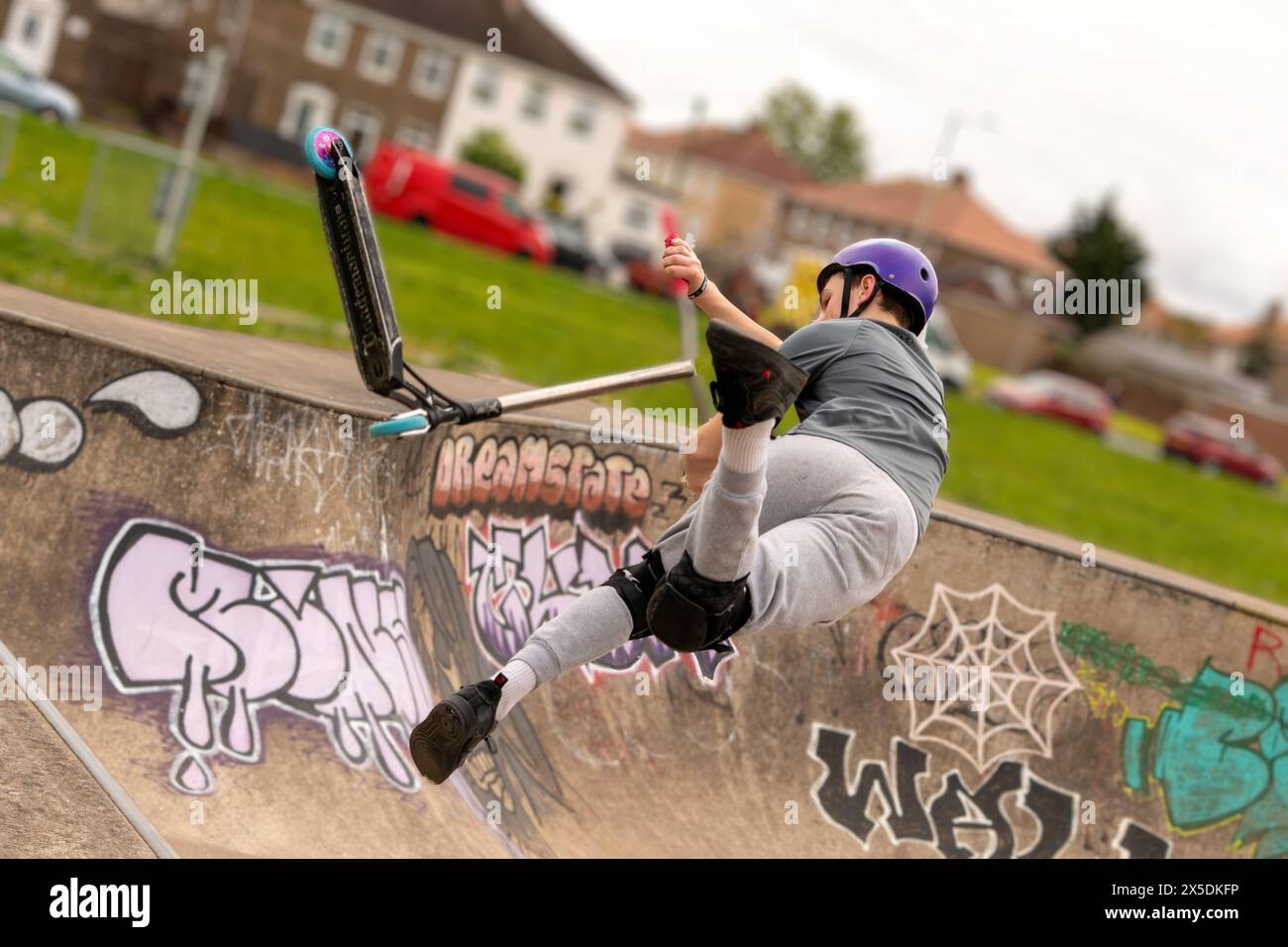 Giovani in camicia verde catturati a mezz'aria facendo acrobazie scooter al Wilderness Skate Park, Porthcawl, Regno Unito. 27 aprile 2024 Foto Stock