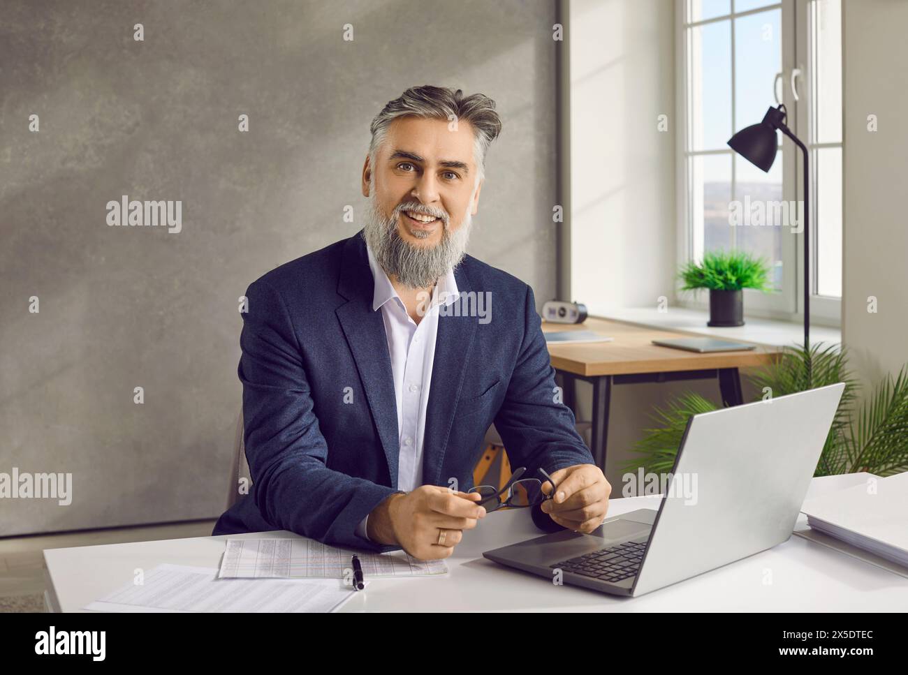 Giovane uomo d'affari che lavora alla scrivania sul posto di lavoro in ufficio, guardando la telecamera sorridente. Foto Stock