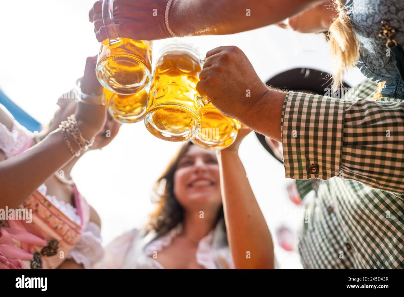Un gruppo di amici brinda con gioia con tazze da birra sotto un cielo luminoso all'Oktoberfest o Dult in germania Foto Stock