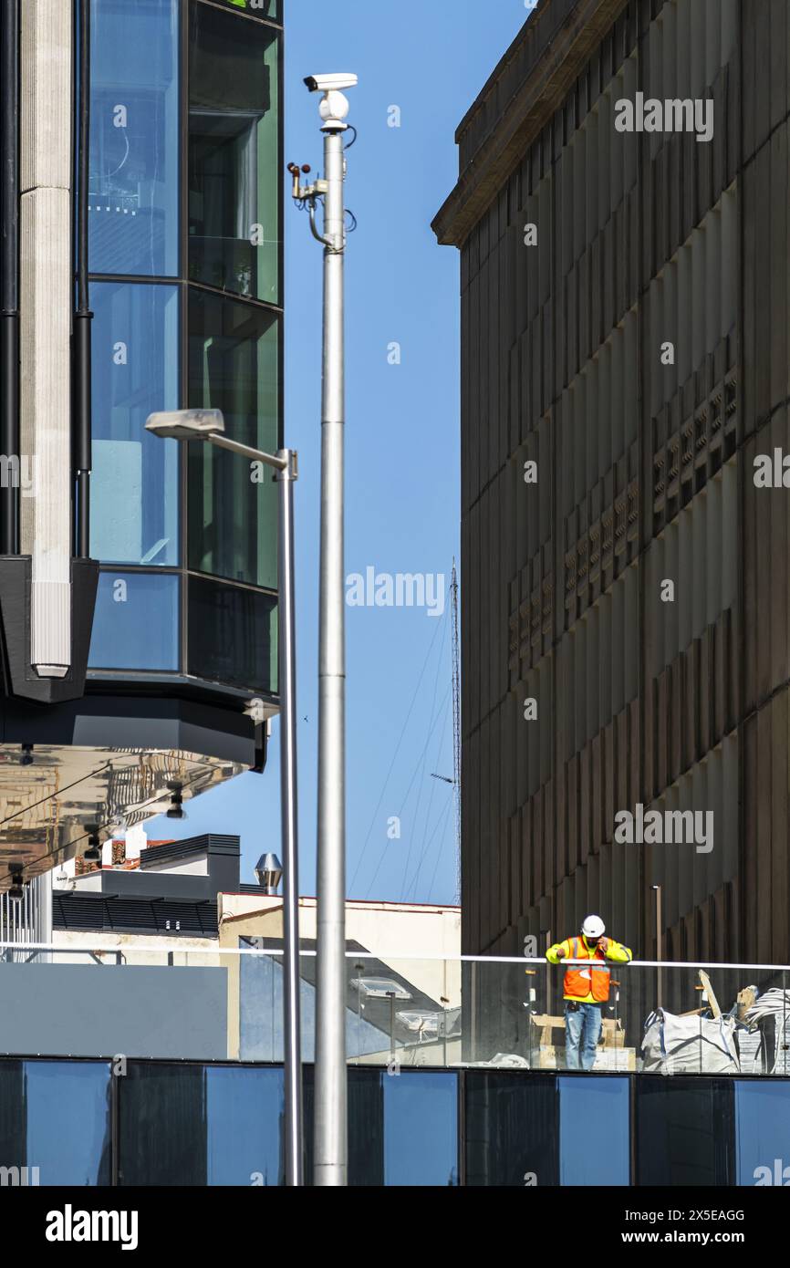Un operaio edile appoggiato alla ringhiera di un edificio in costruzione con facciate in vetro temperato Foto Stock