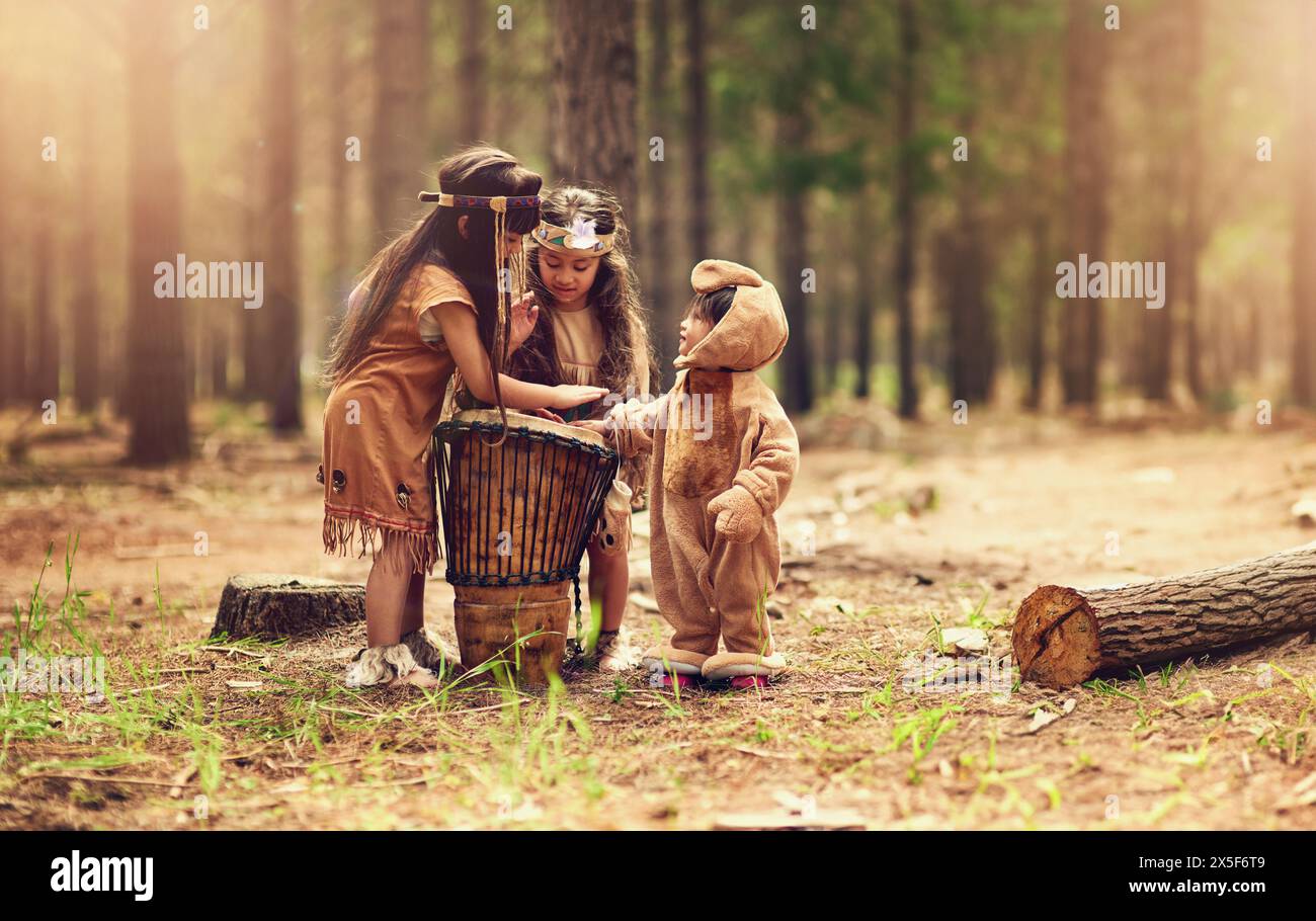Bambini nativi americani, tamburi e felici per la musica suonando, legando e collegando nei boschi. Fratelli, bambini e strumenti con cultura Foto Stock