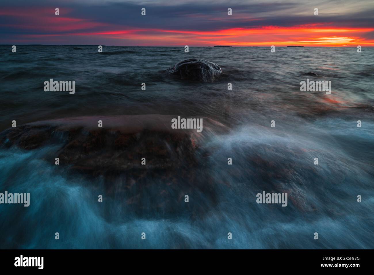 Una massiccia roccia si trova in modo imposabile al centro di un vasto corpo d'acqua, circondato da onde ondulate. La roccia si distingue nettamente contro l'acqua, cre Foto Stock