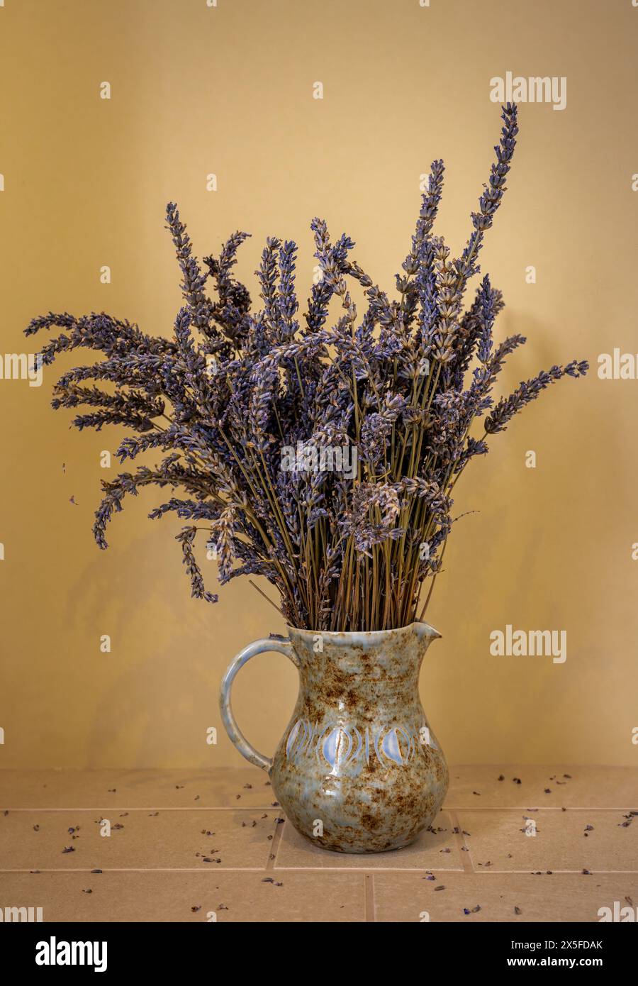 Lavanda secca in una caraffa. Con parete gialla e ripiano piastrellato. Orientamento verticale. Foto Stock