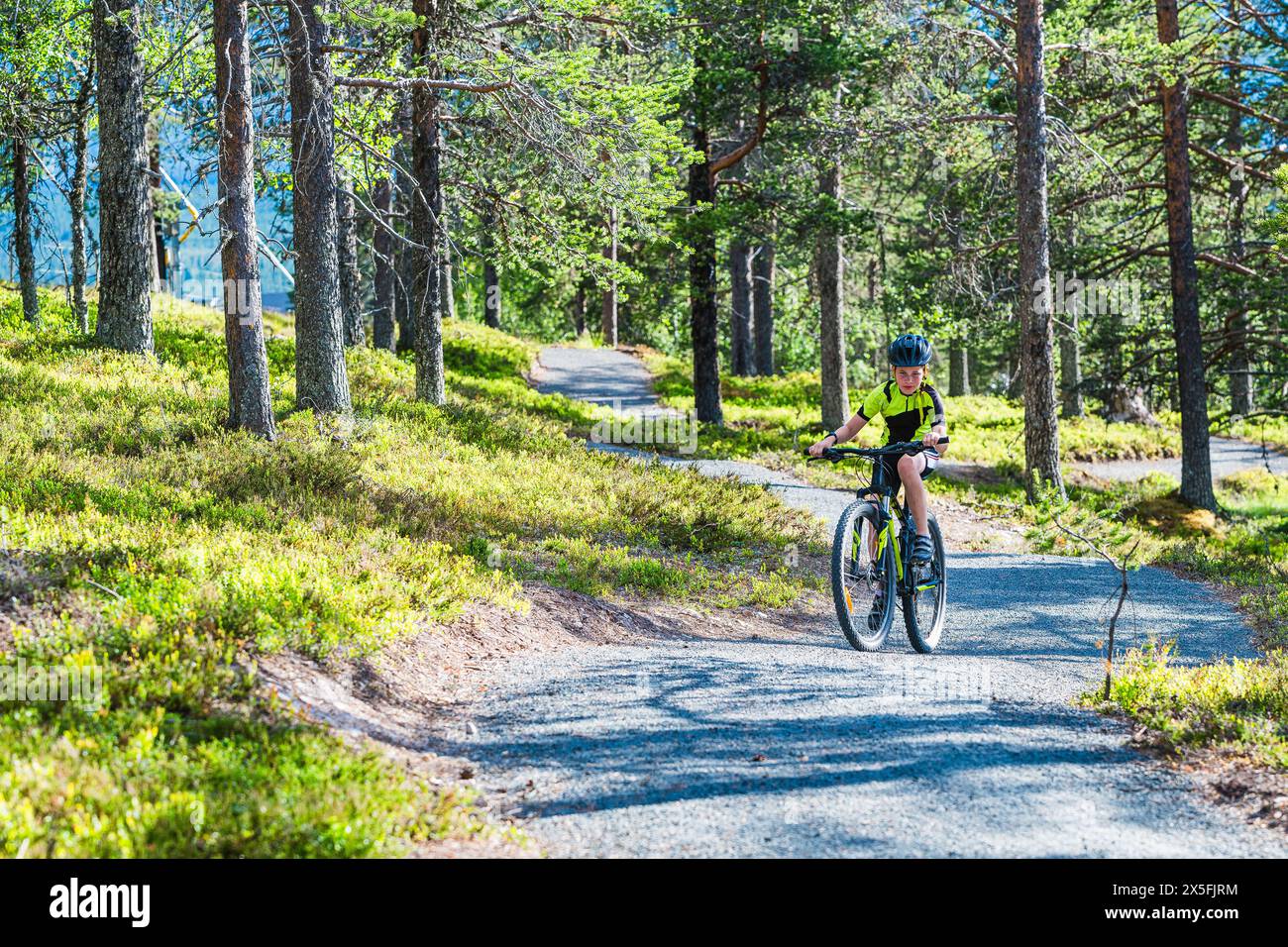 Un giovane ciclista dotato di casco e abbigliamento sportivo pedala con entusiasmo lungo un sentiero tortuoso nella foresta. La scena è racchiusa in Foto Stock