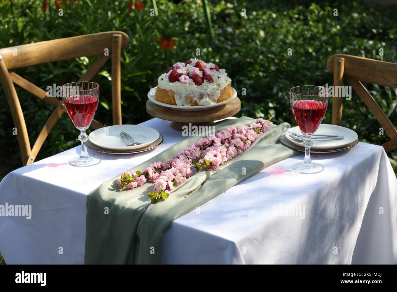 Splendidi fiori primaverili, deliziosa torta e bicchieri da vino sul tavolo in giardino Foto Stock