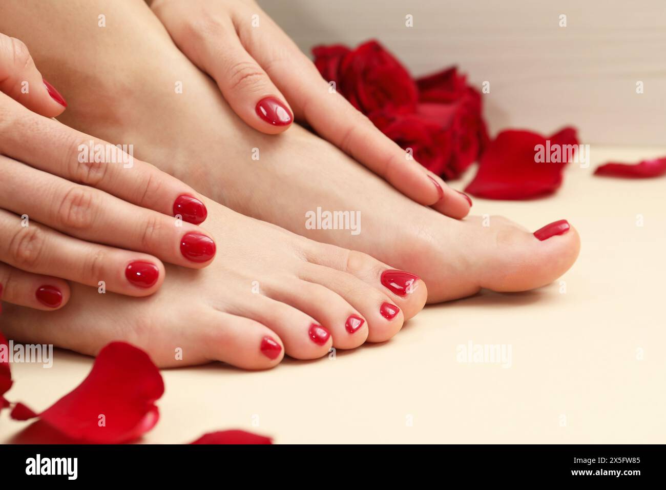 Donna con eleganti unghie rosse dopo la procedura di pedicure e petali di rosa su sfondo beige, primo piano Foto Stock
