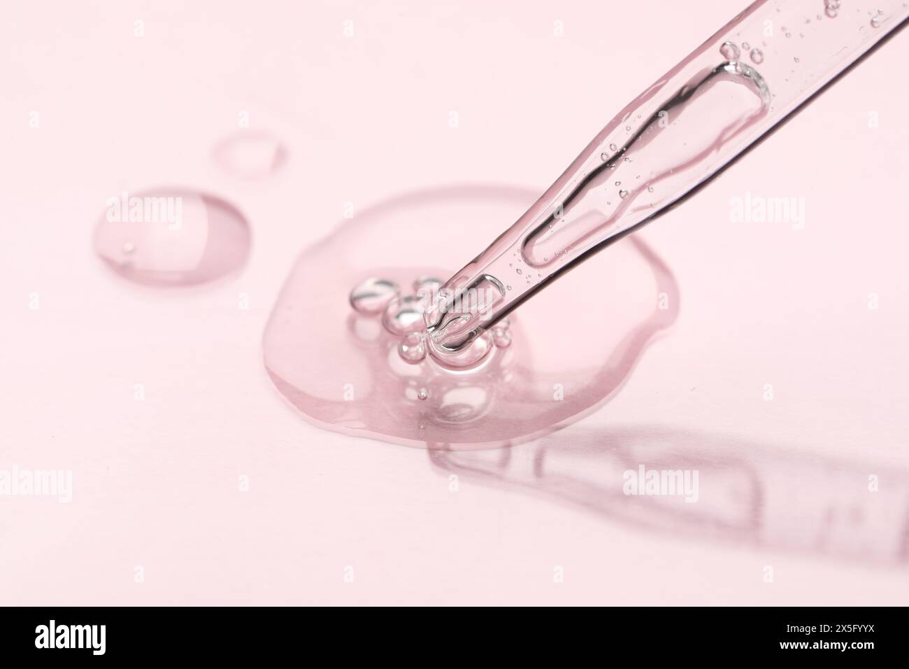 Pipetta in vetro e liquido trasparente su sfondo rosa chiaro, primo piano Foto Stock