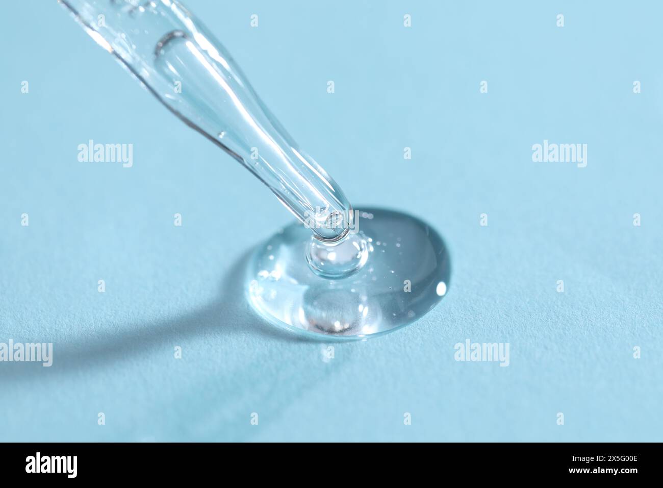 Pipetta in vetro e liquido trasparente su sfondo azzurro, primo piano Foto Stock