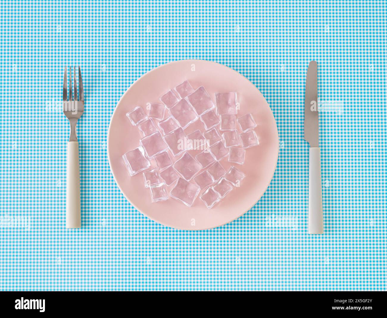 Layout creativo realizzato con piatto rosa, cubetti di ghiaccio, coltello e forchetta su sfondo bianco e blu. Concetto di cibo a zero calorie minimo. Foto Stock