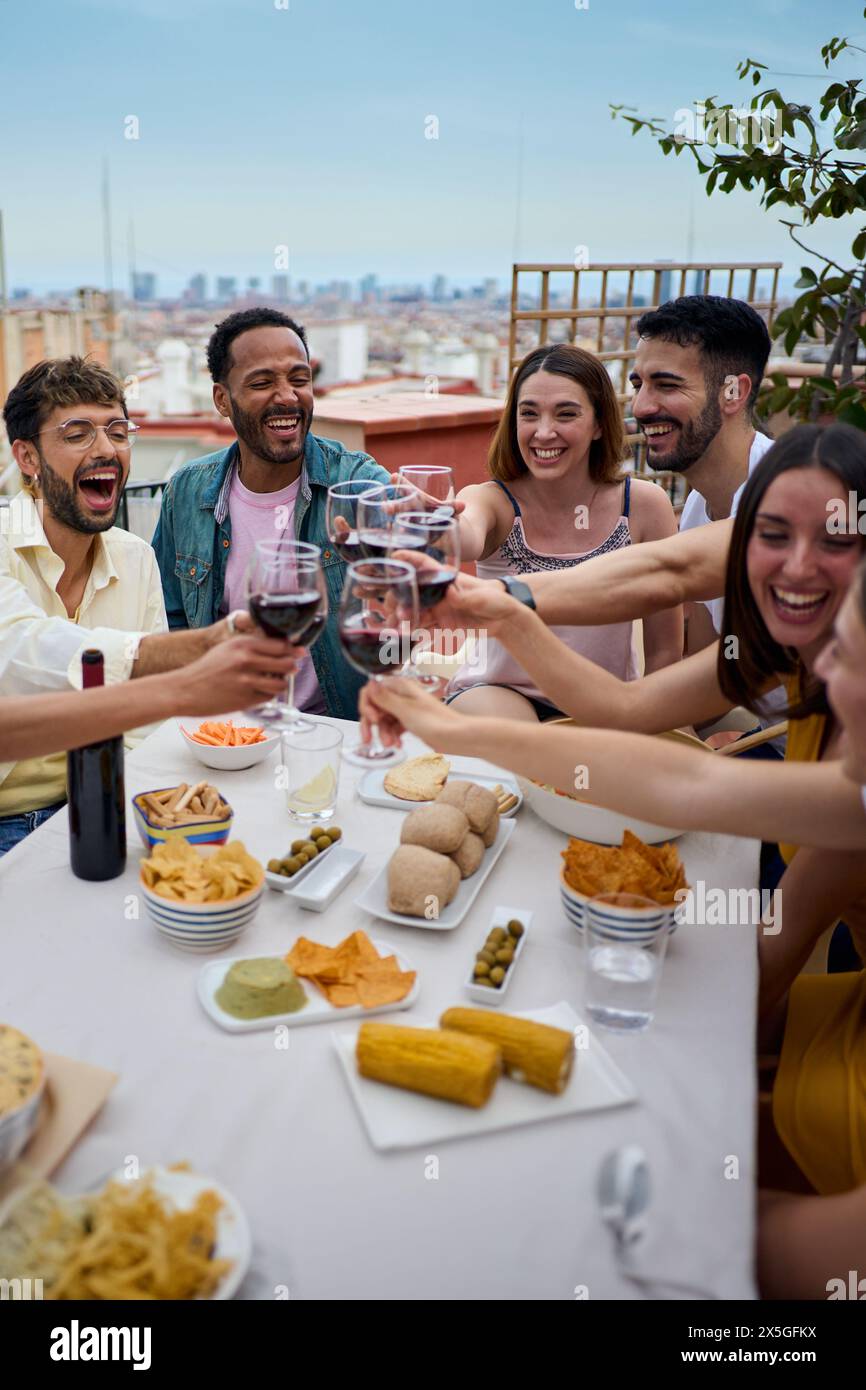 Raduna allegri giovani amici multirazziali, brinda vino rosso e festeggia sul tetto. Foto Stock
