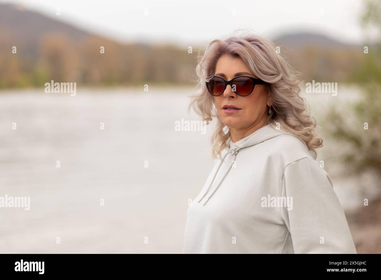 Donna matura con capelli grigi che indossa occhiali da sole sul fiume. Foto Stock