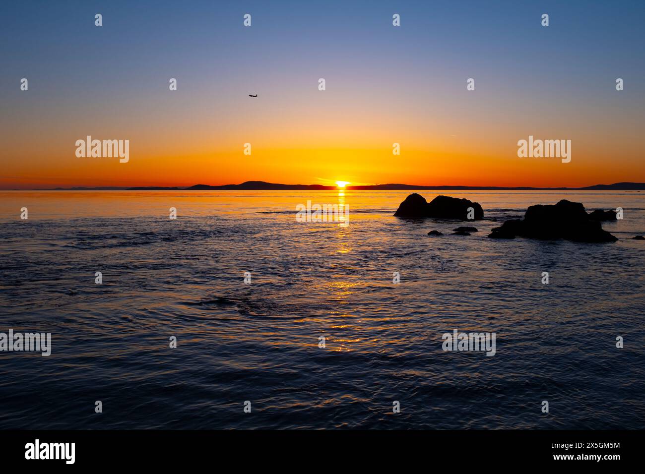 WA24843-00....WASHINGTON - tramonto sullo stretto di Rosario e sul Mare di Salish con un aereo nel cielo. Vista da West Point Beach su Whidbey Island, Foto Stock