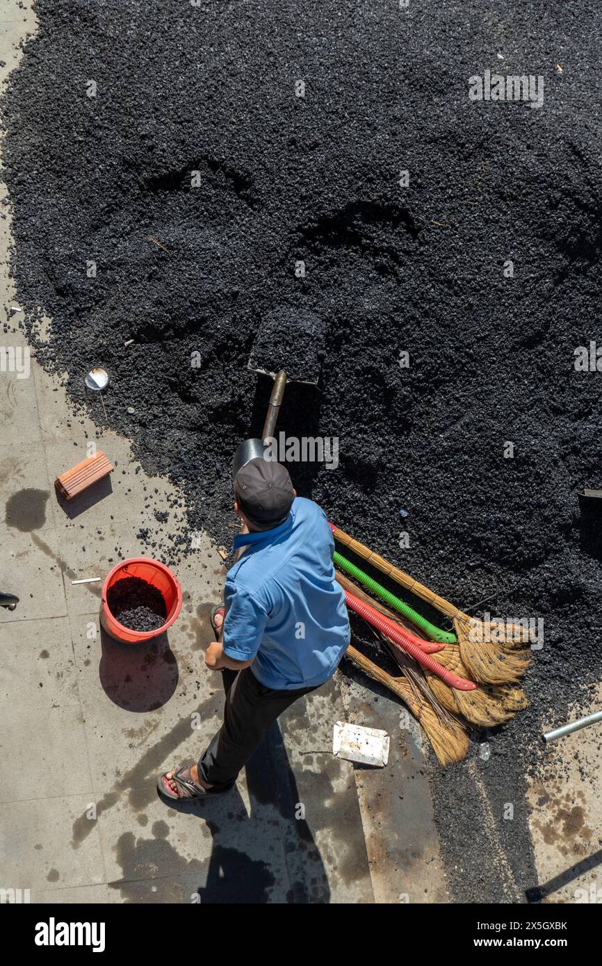 Un lavoratore con una pala carica il materiale da costruzione in una benna Foto Stock