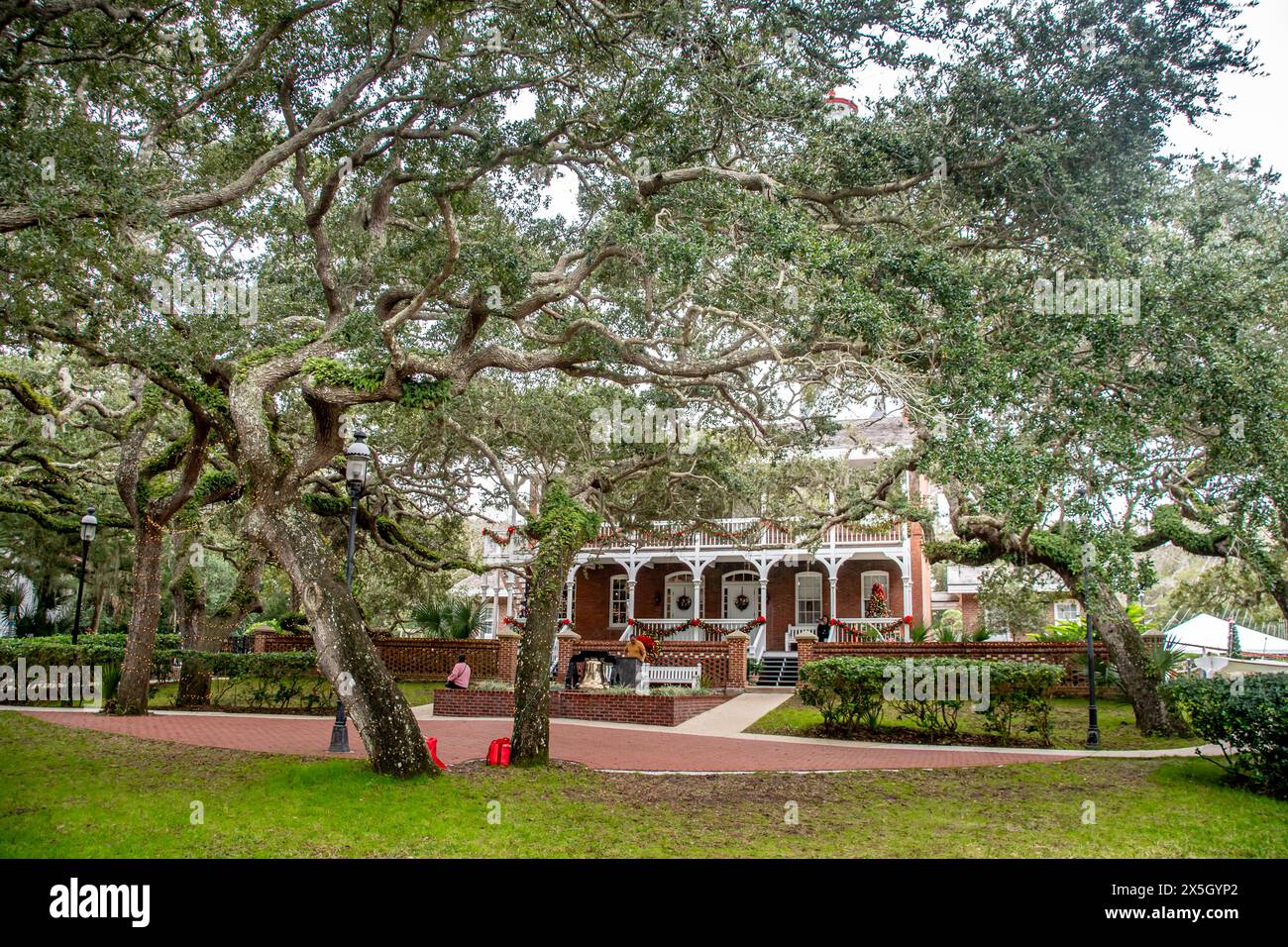 Storico edificio in mattoni a due piani con portici avvolgenti e una campana commemorativa sotto le enormi querce vive a St. Augustine, Florida Foto Stock