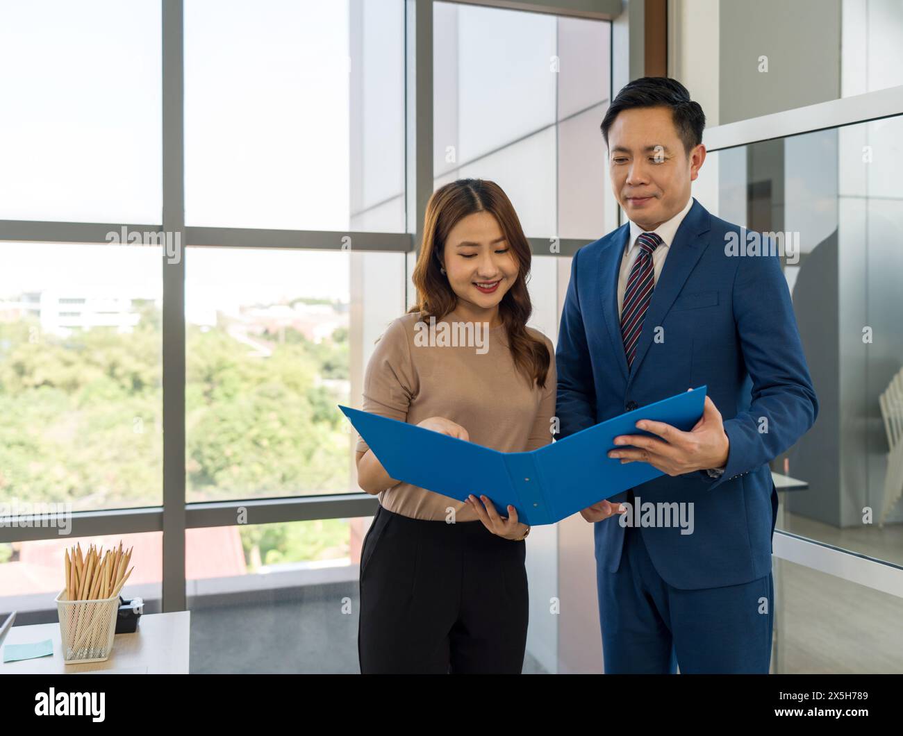 Uno sforzo di lavoro collaborativo, una discussione sul rapporto aziendale. Giovane segretaria e manager in tuta che guarda un documento all'interno di una cartella blu. Sono S Foto Stock