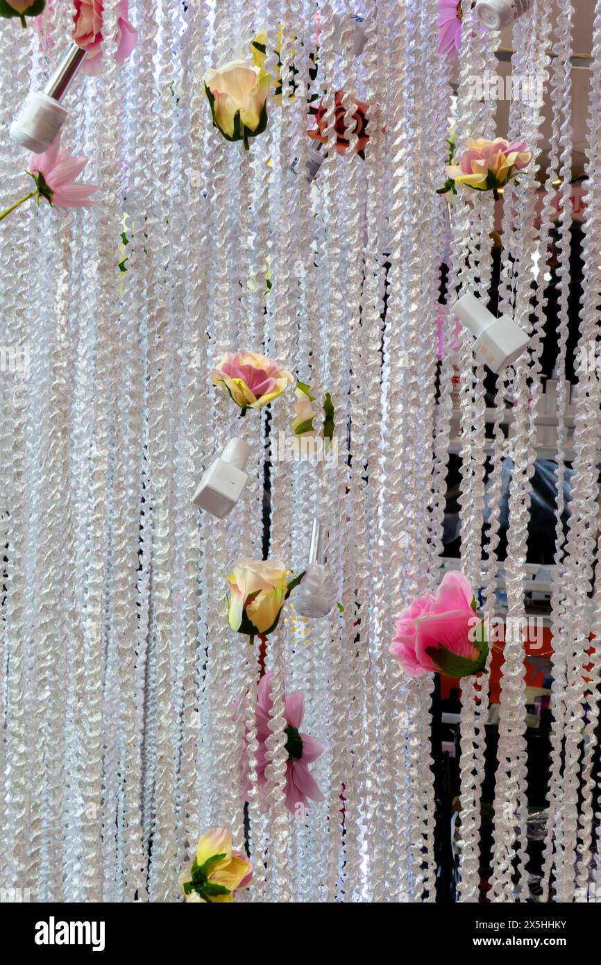 Sfondo con una grande tenda intrecciata bianca fatta di corde intrecciate, decorata con fiori e bottiglie di smalto per unghie. La tenda è appesa ed è decorata Foto Stock