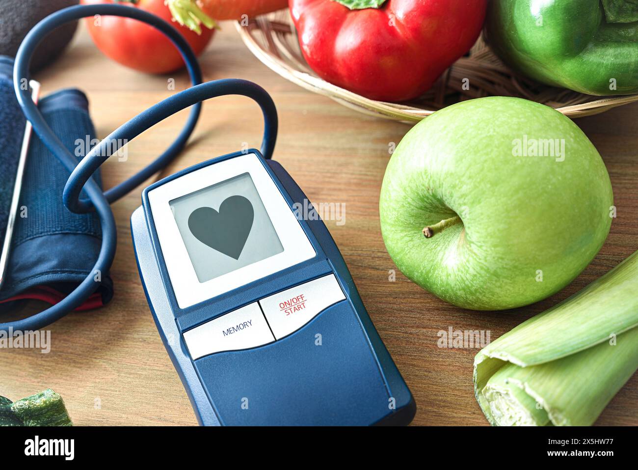 Contesto concettuale di alimentazione sana e pressione sanguigna soddisfacente con misuratore di pressione con cuore su tavola di legno con frutta e vegetab Foto Stock