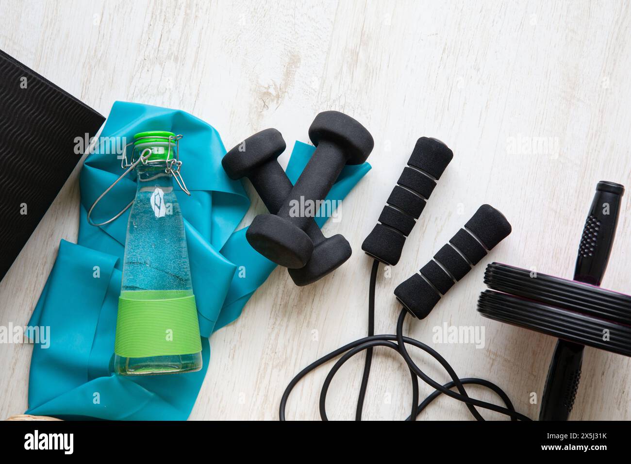 Vari attrezzi per l'allenamento domestico a casa. Tappetino per esercizi, fune da salto, elastico, manubri, bottiglia d'acqua. Foto Stock