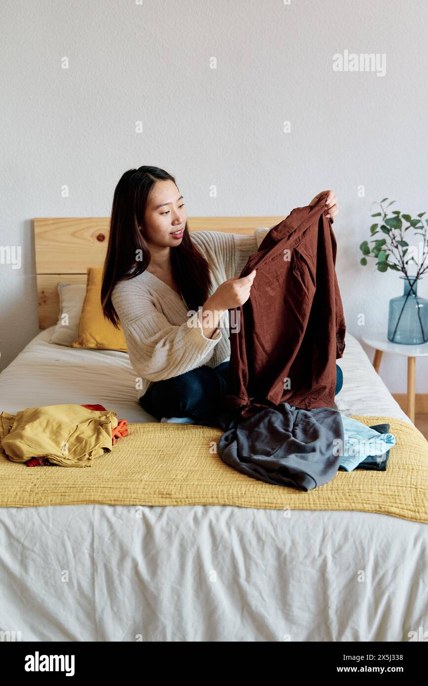 Una donna seduta su un letto mentre tiene in mano una giacca Foto Stock