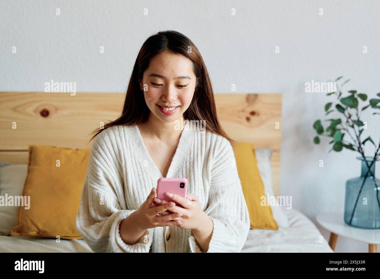 Una donna è seduta su un letto, concentrata sullo schermo del telefono Foto Stock