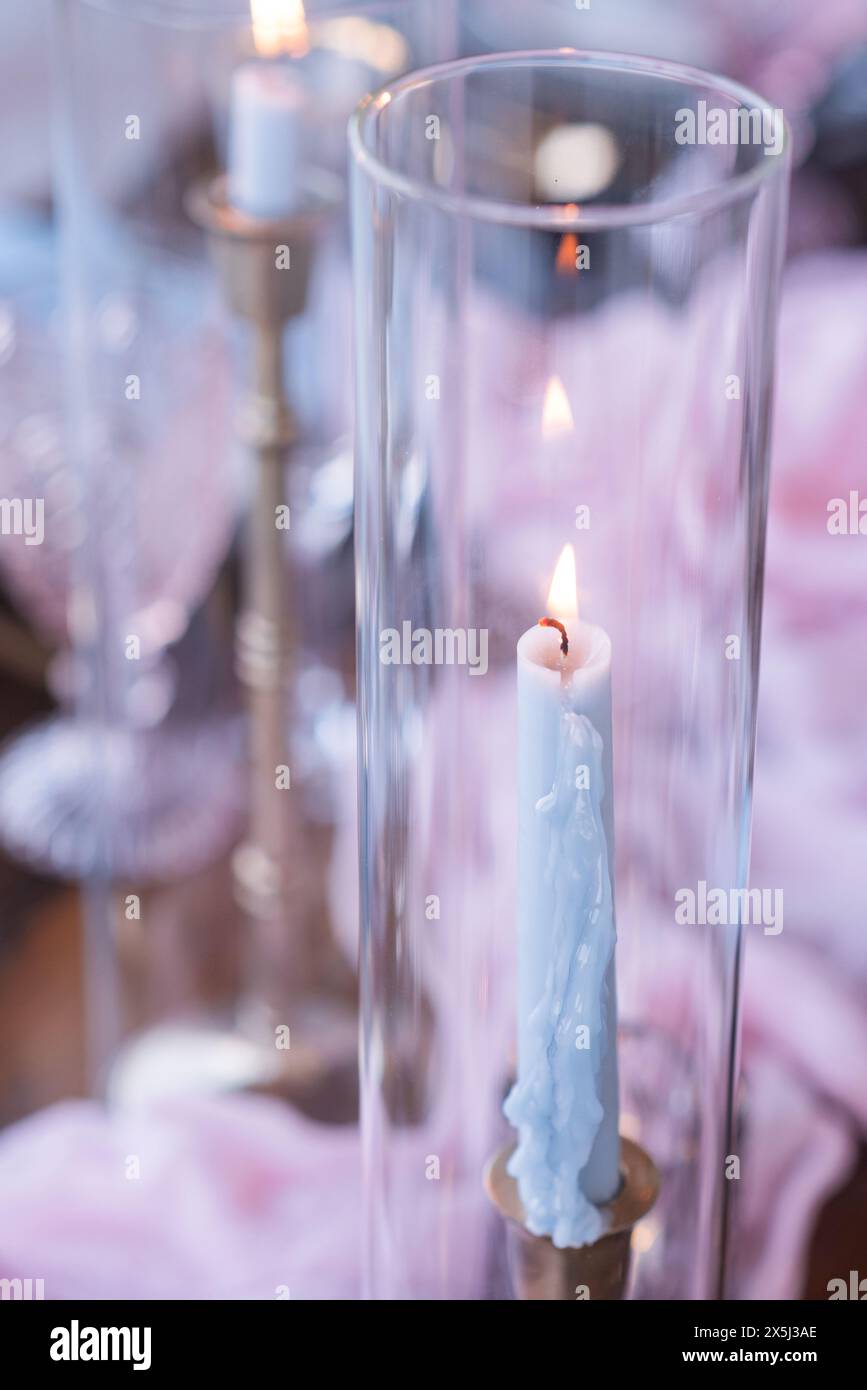 Primo piano di una candela blu illuminata con cera gocciolante, appoggiata contro l'ele Foto Stock