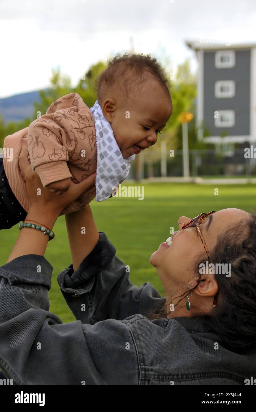 La madre nera solleva il bambino ridendo in un gioioso momento di legame all'aperto Foto Stock