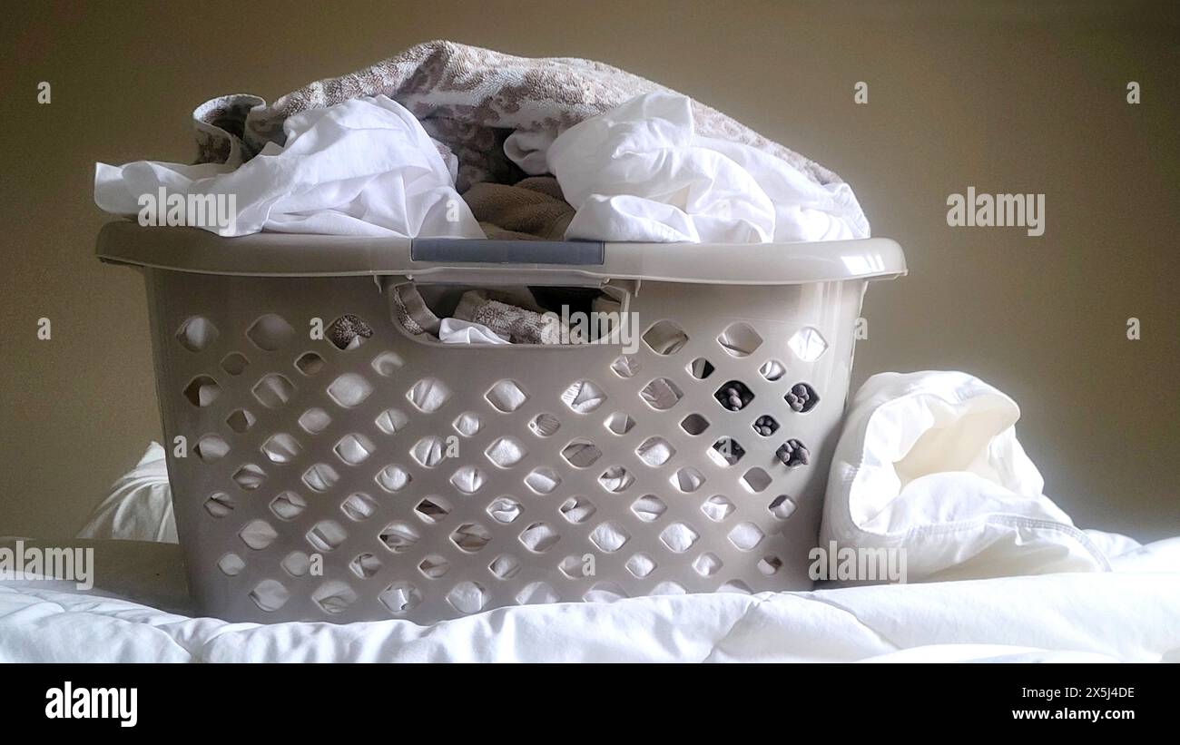 Cestino per bucato pieno di biancheria bianca su un letto Foto Stock